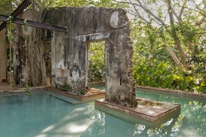 A pool with a rustic, weathered structure in the background, surrounded by lush greenery.