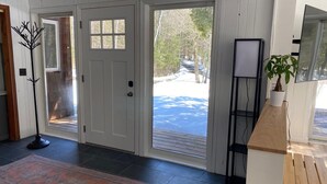 Un hall d’entrée moderne avec un plancher en bois, un tapis à motifs et une vue sur un paysage enneigé, visible à travers des portes vitrées.