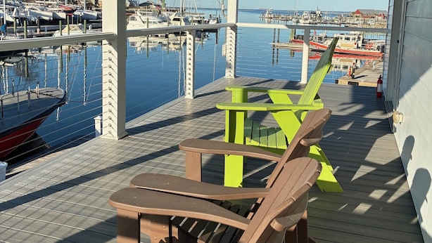 A covered deck with wooden chairs and tables, overlooking a marina with boats. - The Captain's Quarters located in Cape Charles, VA offers breathtaking views. (Cape Charles)