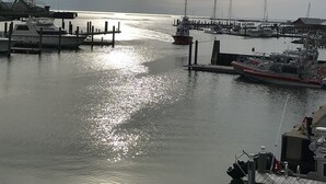 A marina with boats docked at piers, calm water reflecting the sky, and a distant shoreline. - The Captain's Quarters located in Cape Charles, VA offers breathtaking views. (Cape Charles)