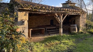 Un bâtiment rustique en pierre, avec un toit en tuiles, un banc en bois et une structure en pierre sur le dessus.