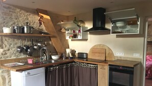 Une cuisine compacte équipée d’un lave-vaisselle, d’une cuisinière et d’un évier. Des casseroles et des poêles sont suspendues au-dessus de l’évier, et une planche à découper en bois est posée sur le plan de travail.