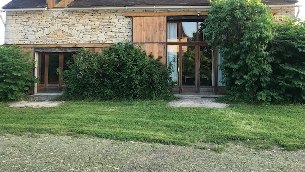 Une maison en pierre avec un toit en pente, des portes en bois et une grande fenêtre en verre.