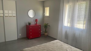 Une chambre à coucher avec un lit, une commode, un miroir, une fenêtre avec des rideaux et une plante en pot.