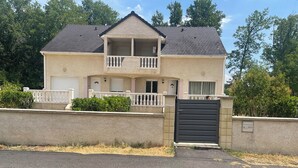 Une maison à deux étages avec un balcon, un garage et une entrée fermée par un portail.