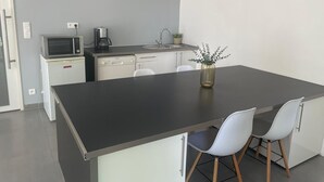 Une cuisine moderne avec un îlot central, des meubles blancs, un four à micro-ondes, une machine à café et une horloge murale.