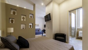 A bedroom with a bed, a TV, a sofa, and a sliding glass door leading to a bathroom.