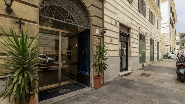 A hotel entrance with a blue door, a potted plant, and a visible car parked outside.