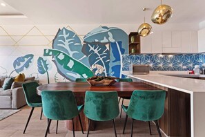 Une cuisine moderne dotée d’un îlot central, de chaises en velours vert et d’un revêtement mural à motifs géométriques.