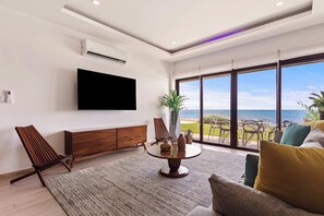 A modern living room with a flat-screen TV, wooden furniture, a round coffee table, and a view of the ocean.