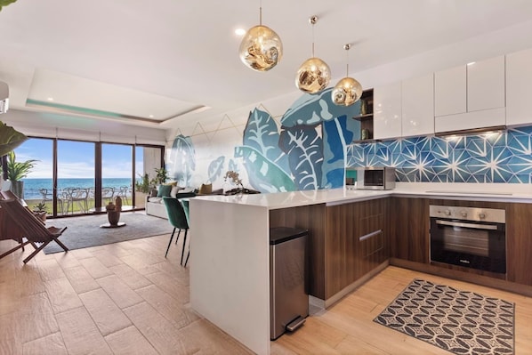 Una cucina moderna con vista sull'oceano, una zona pranzo panoramica e un soggiorno con una grande pianta.