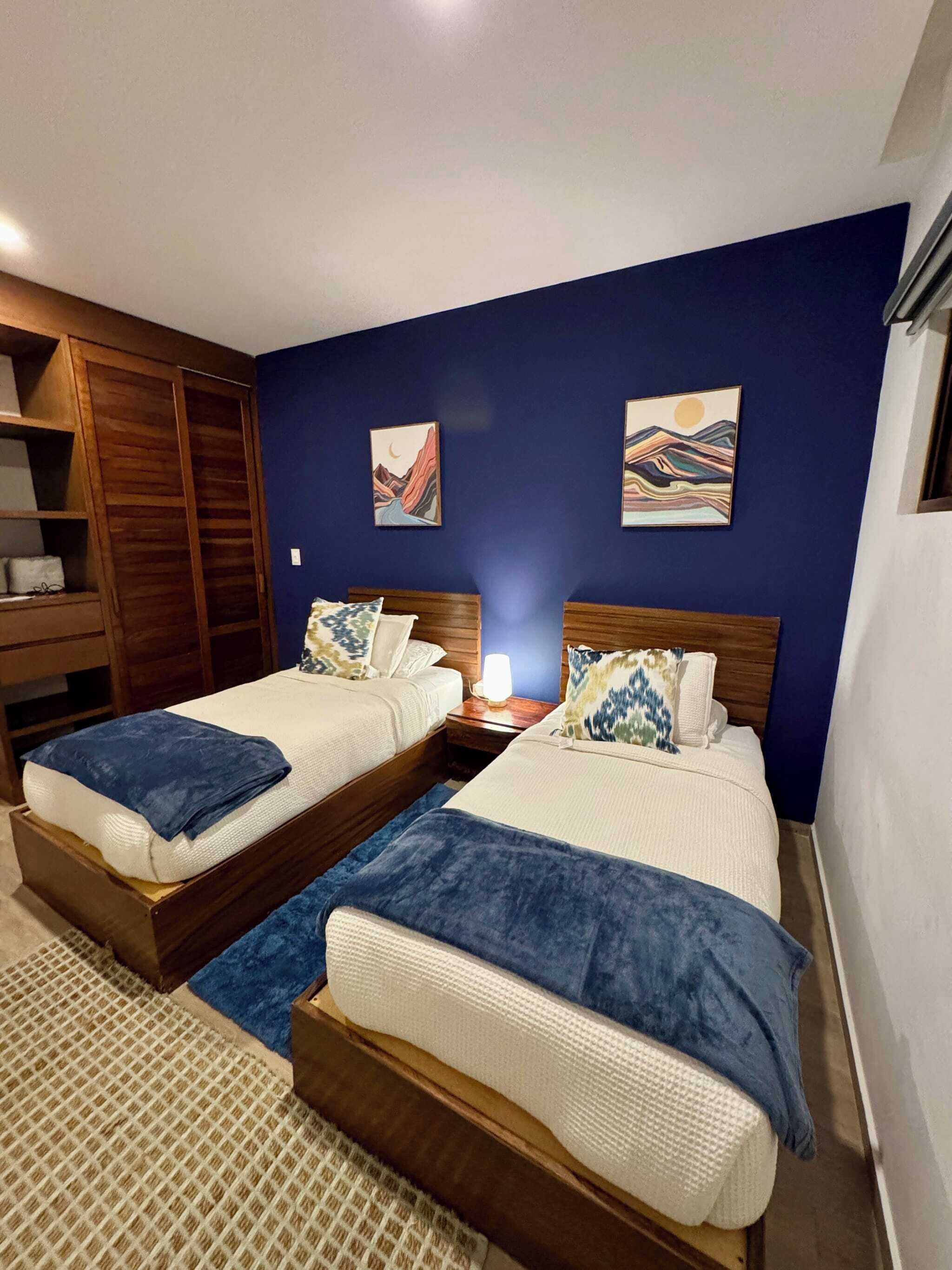A hotel room with two beds, a wardrobe, and artwork on the walls.
