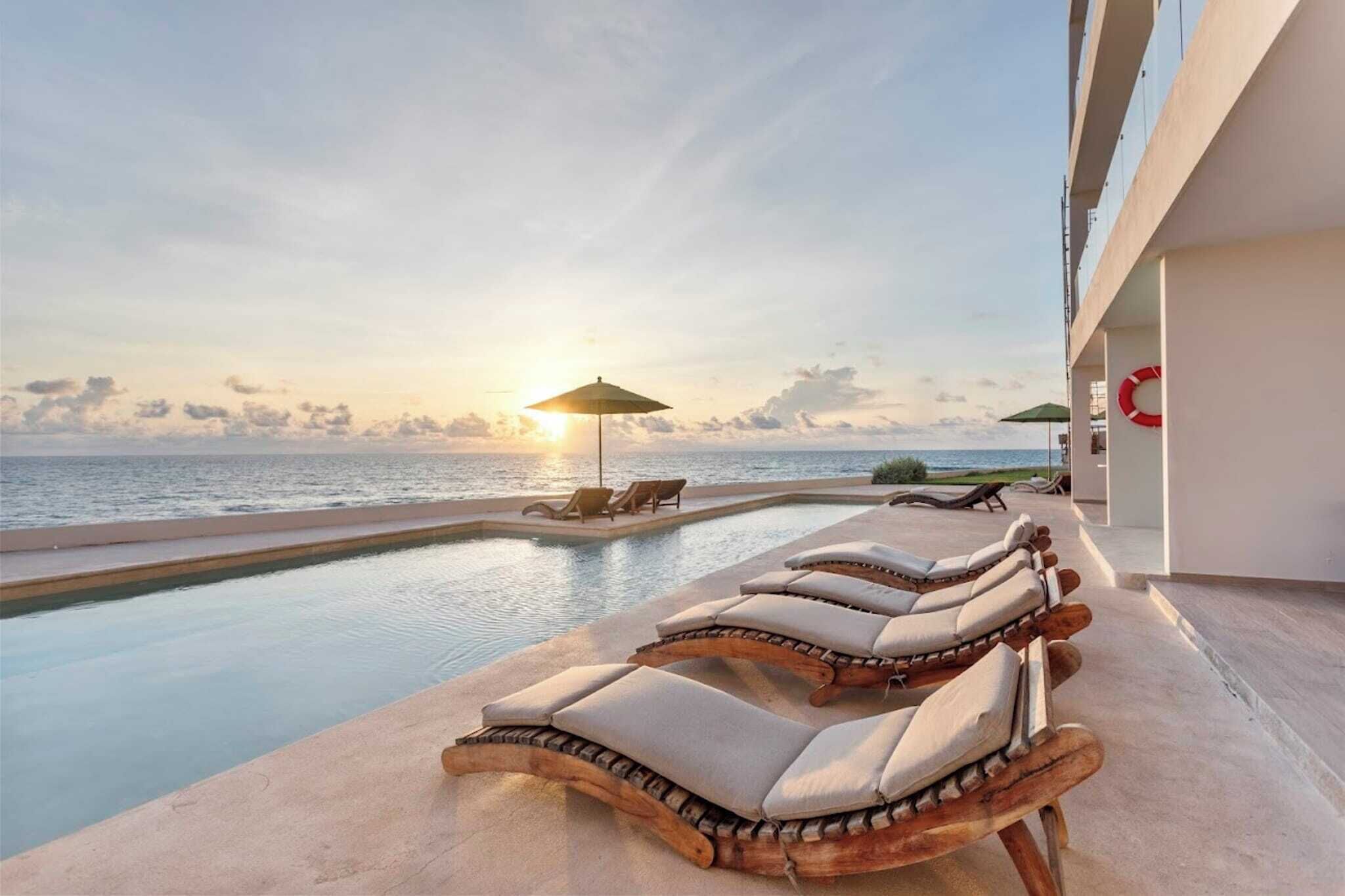 A poolside area with lounge chairs and a view of the ocean at sunset.