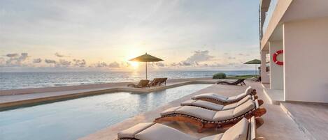 A poolside area with lounge chairs and a view of the ocean at sunset.