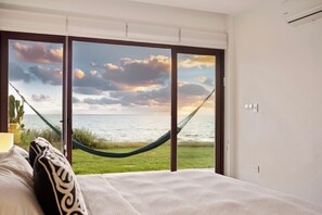 A bedroom with a large window, a hammock, and a view of the sea.
