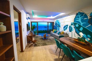 Un soggiorno moderno con vista sull'oceano, una zona pranzo con tavolo in legno e un grande murale.