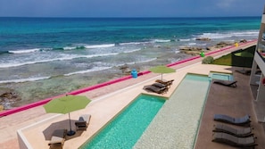 Un espace piscine doté de chaises longues et de parasols, avec vue sur l’océan.
