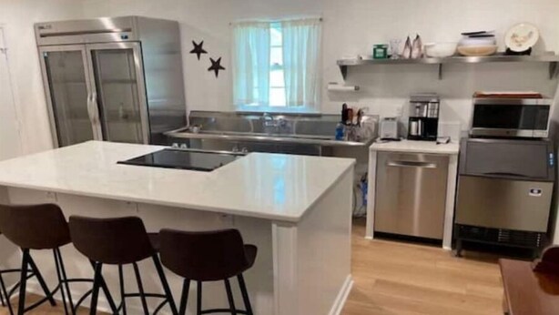 A modern kitchen with a central island, bar stools, a refrigerator, a microwave, and a dishwasher.