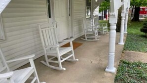 A porch with white rocking chairs and a white door.