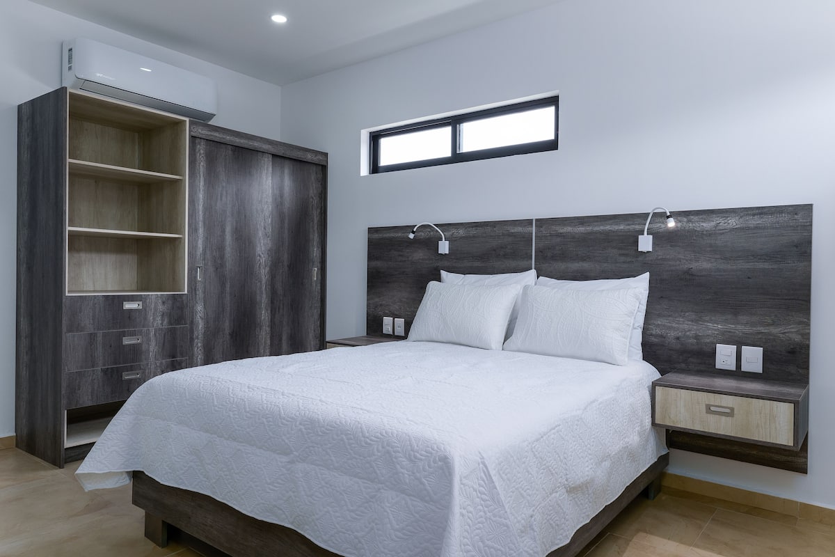 Une chambre moderne avec un grand lit, une armoire intégrée, des tables de chevet et une petite fenêtre.