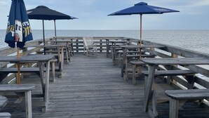 A wooden pier with tables and benches, some with umbrellas, extending towards the water.