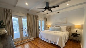 Un dormitorio con una cama grande, un ventilador de techo y vistas al exterior a través de las ventanas.