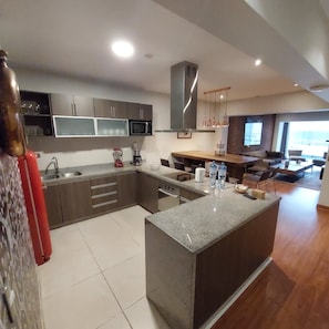 A modern kitchen with a central island, built-in appliances, and a dining area with a view. - Larcomar Luxury Penthouse (Miraflores)