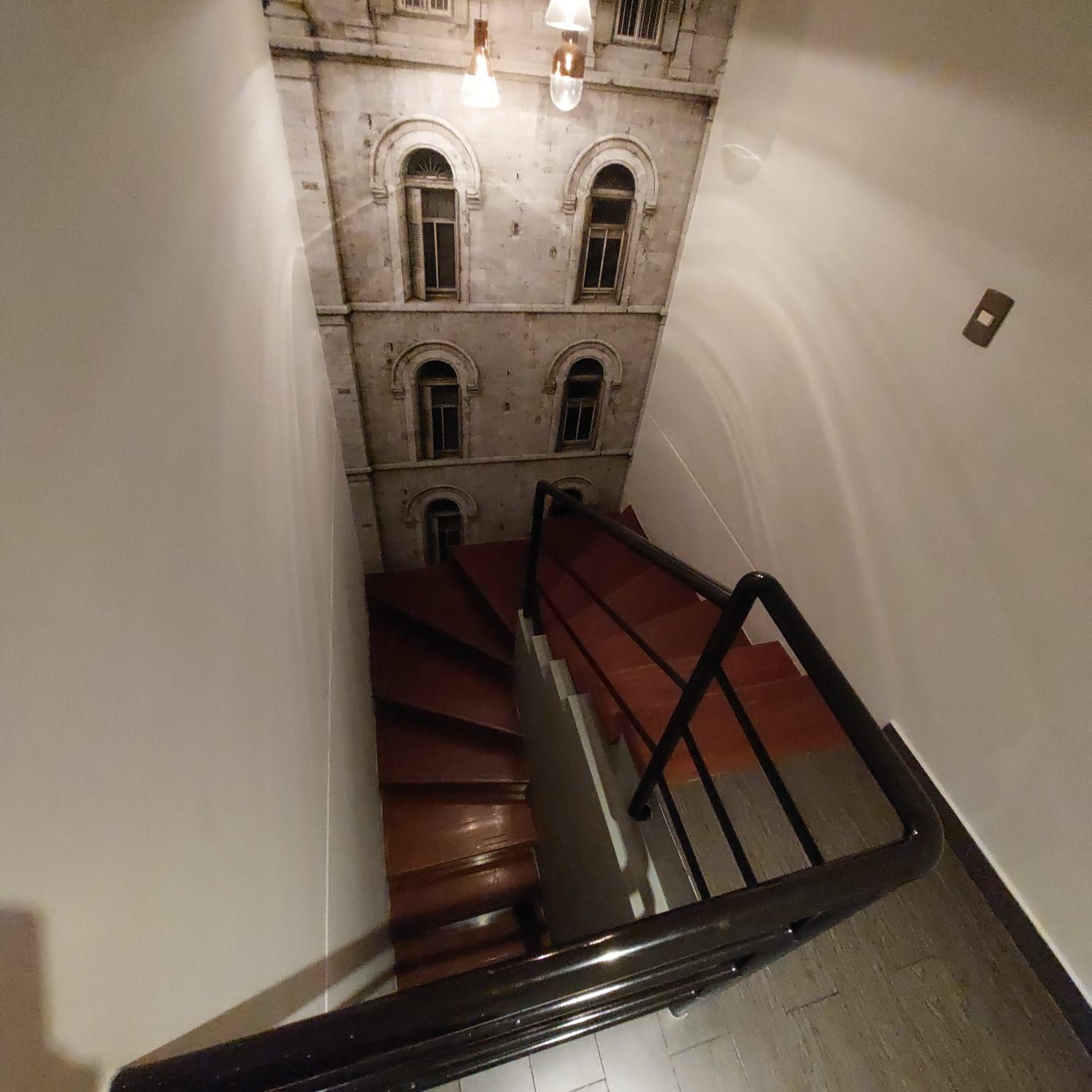 A staircase with a handrail leading to a building with multiple windows and a light fixture above.