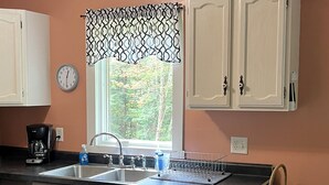 A kitchen with a double sink, dark cabinets, a clock, and a window with a patterned valance. - Go out on an Adventure! Relax & Unwind at our cozy & quiet location.Pet Friendly (Munising)