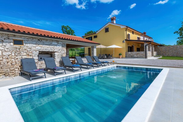 A swimming pool with lounge chairs, a stone building, and a yellow house with a red roof. - Rückzugsort am Meer mit Pool, nur Wenige Minuten vom Strand Entfernt (Trget)