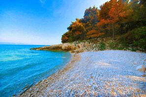 A pebble beach with clear blue water and autumn-colored trees in the background. - Rückzugsort am Meer mit Pool, nur Wenige Minuten vom Strand Entfernt (Trget)