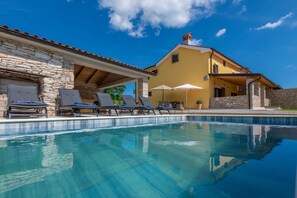 A pool area with lounge chairs and umbrellas, a stone building with a yellow facade, and a clear blue sky. - Rückzugsort am Meer mit Pool, nur Wenige Minuten vom Strand Entfernt (Trget)