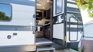 Una vehículo recreativo con zona de cocina, unos escalones que conducen a la entrada y un felpudo.