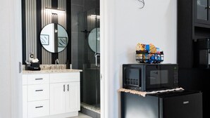 Eine moderne Küche mit einem schwarzen Kühlschrank, einer Mikrowelle und einer Kaffeemaschine. Ein weißes Schranksystem mit Spiegel befindet sich über dem Spülbecken.