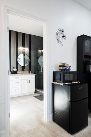 A modern kitchen with a black refrigerator, microwave, and coffee maker. There is a white cabinet with a mirror above the sink.