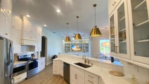 Een moderne keuken met witte kasten, roestvrijstalen apparatuur en hanglampen.