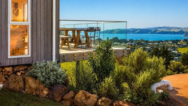 Una casa moderna con balcón de vidrio con vista a una bahía pintoresca.
