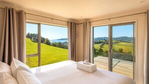 Habitación de hotel con una cama grande, dos ventanas y vistas a un paisaje verde.