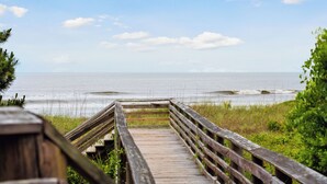 Una passerella di legno conduce a una spiaggia, con vista libera sull'oceano e sul cielo.