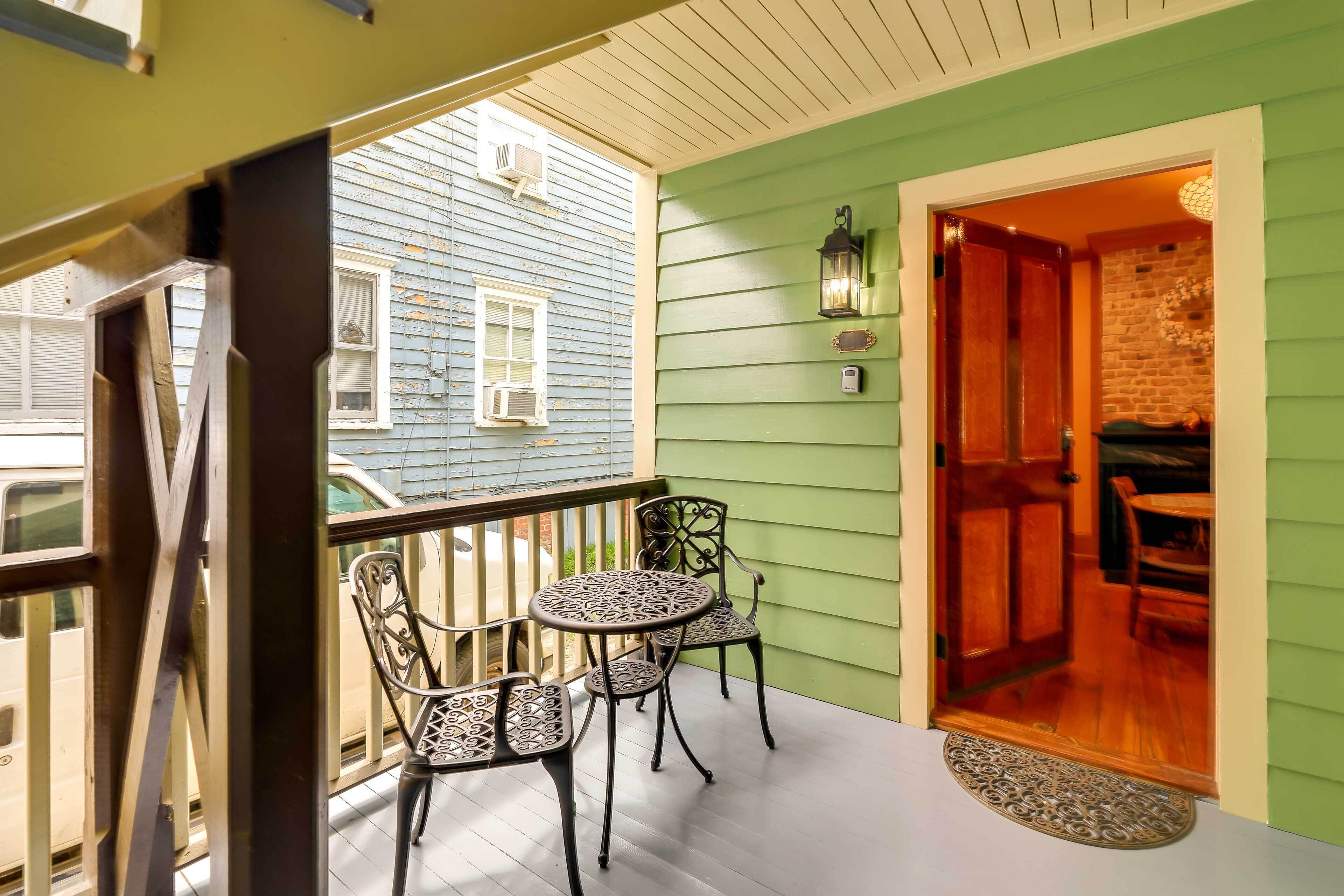 A balcony with a table and chairs, a door leading inside, and a view of a neighboring house.