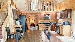 Un interior espacioso de madera con una mesa de comedor central, zona de cocina y una escalera.