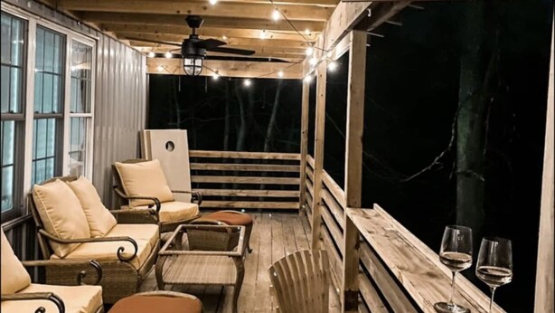 Un rincón acogedor en el porche con muebles de mimbre, un taburete de bar y dos copas de vino sobre el alféizar.