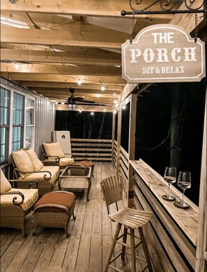Un rincón acogedor en el porche con muebles de mimbre, un taburete de bar y dos copas de vino sobre el alféizar.