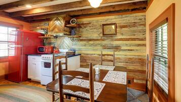 Una cocina rústica con paredes de madera, un refrigerador rojo, armarios blancos y una mesa de comedor con sillas.