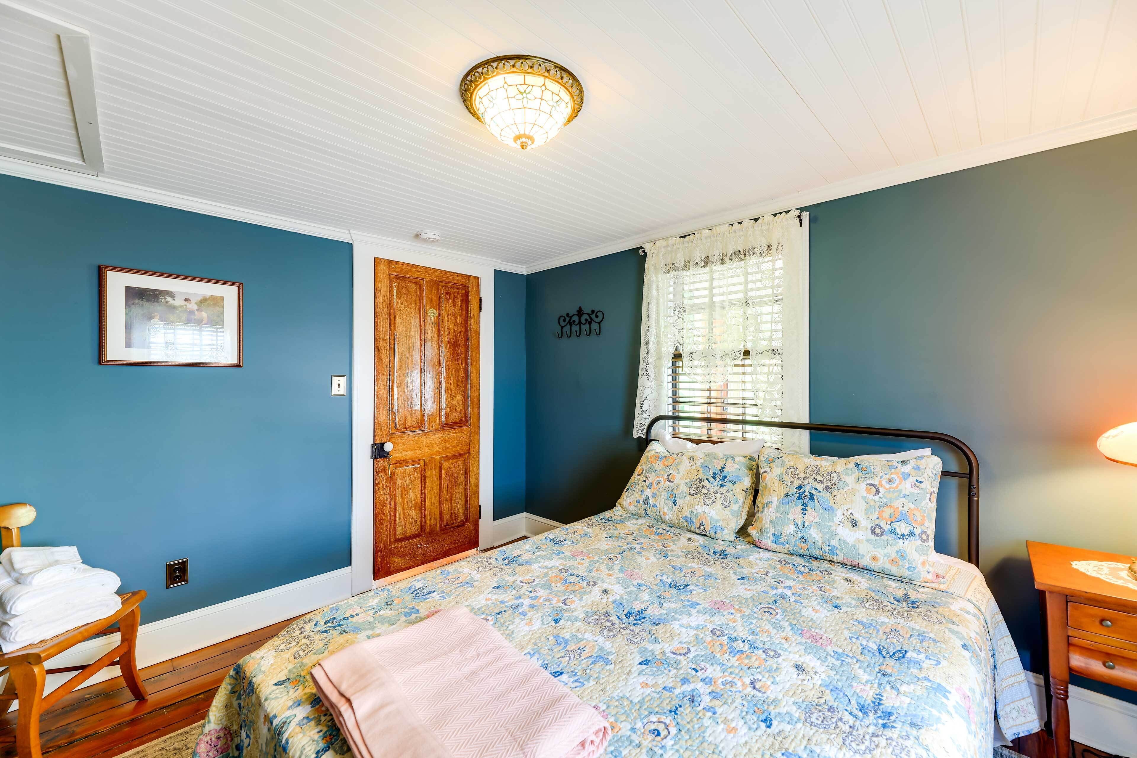 A bedroom with a bed, a wooden door, a framed picture on the wall, and a window with curtains.