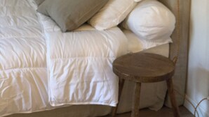 A bedroom with a bed, pillows, a hanging light fixture, and a wooden stool. - Studio in the historic center (Ajaccio)