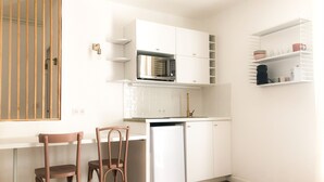 A compact kitchen with white cabinets, a microwave, and a refrigerator. There are two wooden chairs and a small shelf with kitchen items. - Studio in the historic center (Ajaccio)
