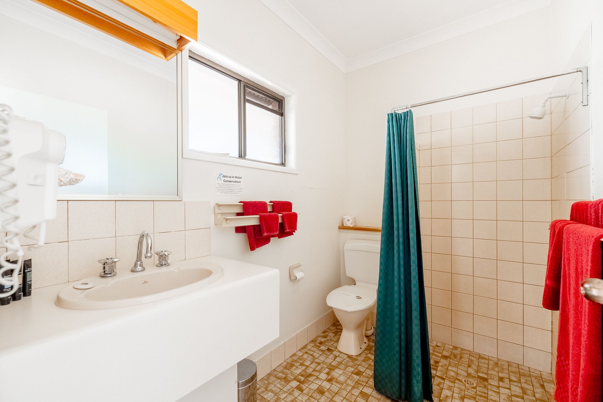A bathroom with a white sink, a toilet, and a shower with a teal curtain.