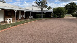 A building with a covered porch, a gravel driveway, and a palm tree. - Landsborough Lodge Motel (Barcaldine)
