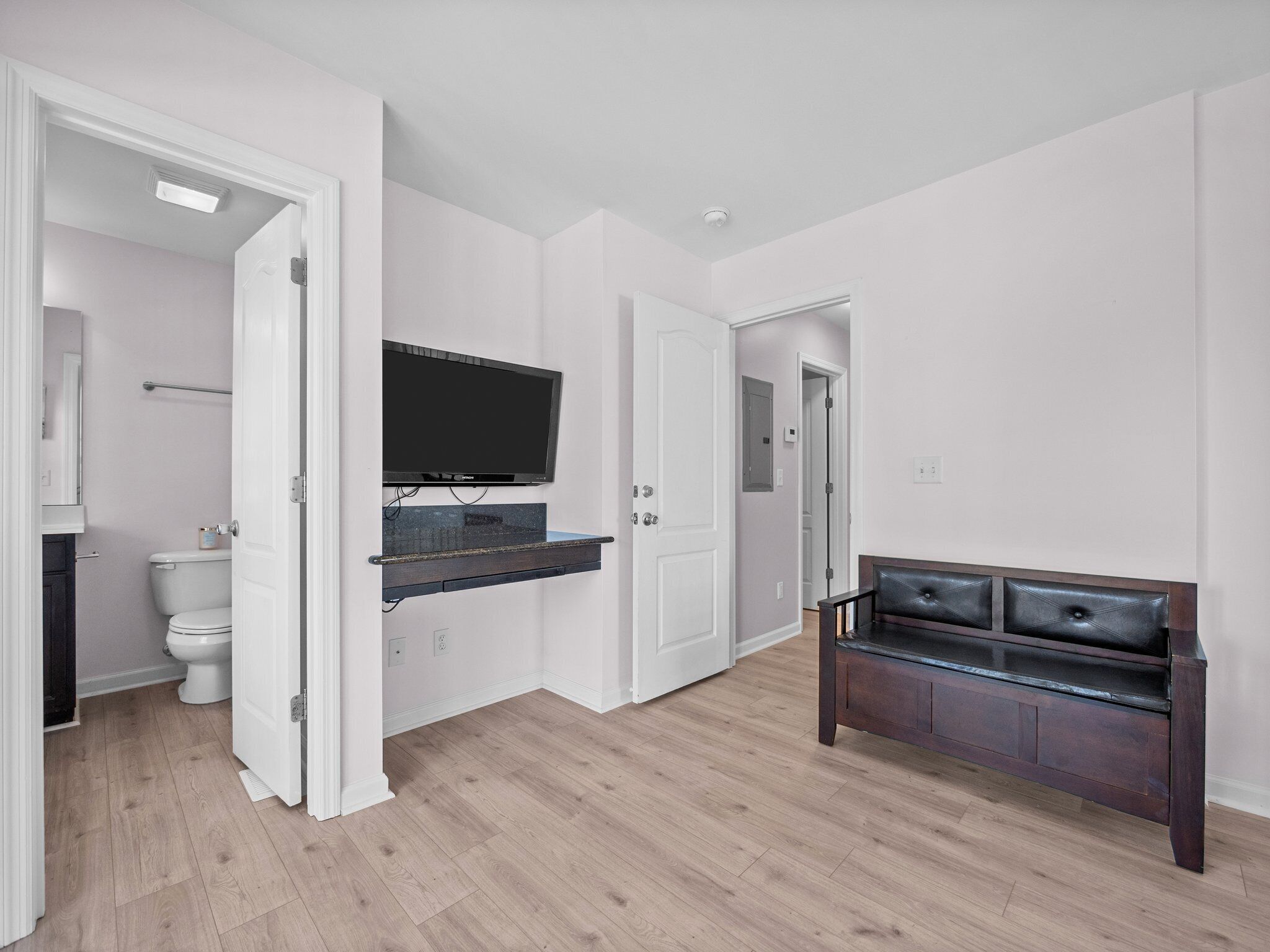 Un bagno moderno con WC, lavandino e specchio. C'è una TV montata a parete e una panca nell'angolo.